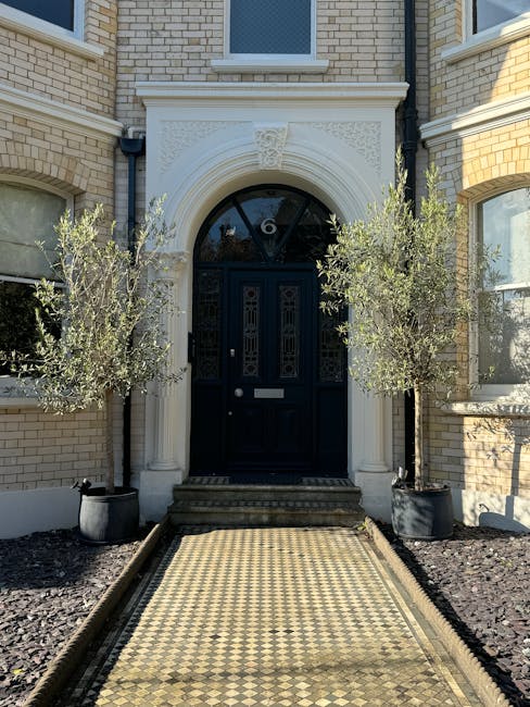 The entrance to a Victorian-style townhouse with a dark blue front door set into an ornate white stone archway featuring decorative carvings and a semi-circular fanlight window above. Flanking the doo